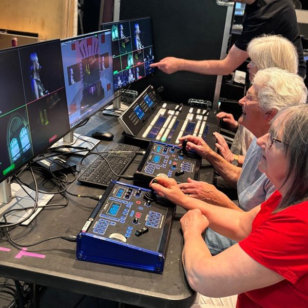 People using video production equipment and control panels while viewing multiple camera feeds on monitors during a technical workshop.