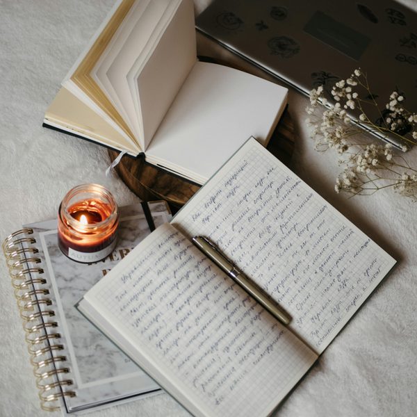 Several books and a laptop laid out on a fabric surface next to a candle