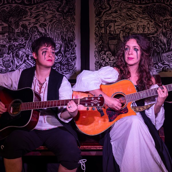 The members of Sh!t Theatre playing guitars on stage, with black tears dripping from their eyes.