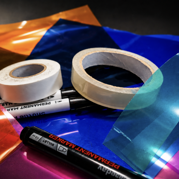 Rolls of tape and permanent markers arranged on colourful translucent plastic sheets in blue, orange, pink and red.